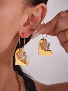 Gros plan de boucles d'oreilles cœur doré avec une fleur en résine sur un modèle
