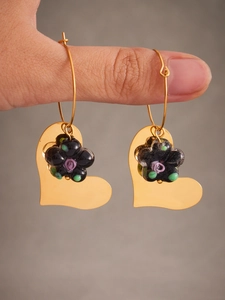 Détail de boucles d'oreilles cœur doré avec fleurs en résine noire et verre coloré