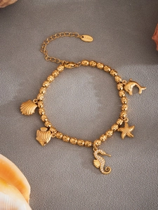 Detailed view of a gold marine charm bracelet with sea horse and starfish on grey texture