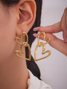 Detail of 18k gold plated double heart dangle earrings worn by a model in soft lighting
