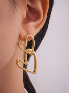 Detail of three-tier golden heart-shaped drop earrings worn by a model in soft lighting