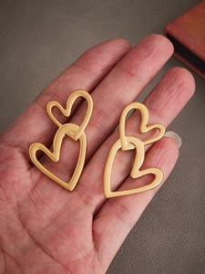 Detail view of interlocking golden heart earrings held in hand for size reference