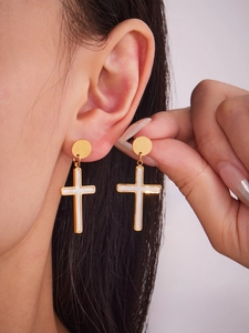 Dettaglio di orecchini a croce in oro 18k con conchiglia indossati e tenuti in mano
