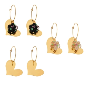 Trois paires de boucles d'oreilles cœur dorées avec détails floraux en résine sur blanc