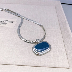 Macro shot of silver-toned necklace featuring an oval pendant with deep blue enamel inlay