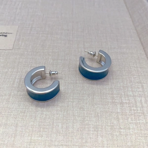 Detailed close-up of C-shaped silver earrings with deep blue liquid enamel coating