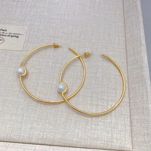 Elegant gold hoop earrings with white pearls on beige textured background, 45-degree view