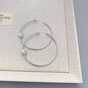 Minimalist silver hoop earrings with white pearl accents on beige textured jewelry tray