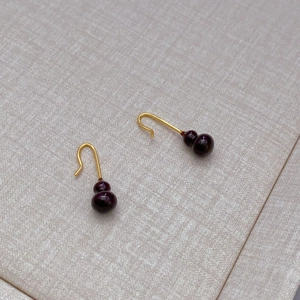 Elegant gold hook earrings featuring deep red enamel gourd pendants on a grey textured background