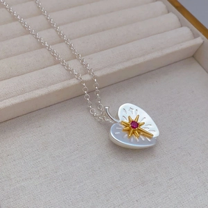 Detailed view of silver heart pendant with golden starburst and red gemstone on linen