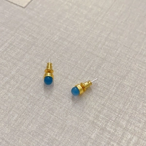 Makroansicht minimalistischer Goldohrringe mit himmelblauen Achatkugeln auf hellem Stoff