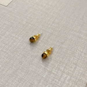 Minimalistische runde Tigerauge-Ohrstecker mit Goldfinish auf grauem texturiertem Hintergrund