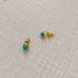 Minimalistische goldene Ohrstecker mit blauen Achatsteinen auf grauem Stoffhintergrund