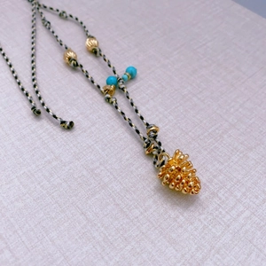 Handmade woven rope necklace featuring a gold pinecone pendant and turquoise beads