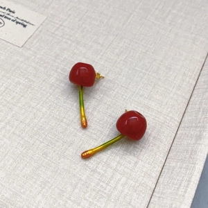 Pastel cherry earrings with glossy red finish and green stems on textured paper