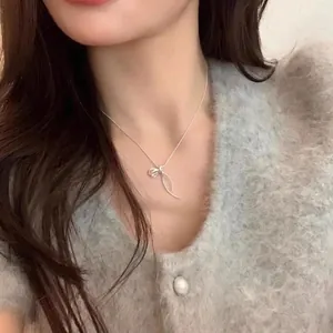 Elegant silver ribbon bow pendant necklace worn by a model on a soft grey sweater