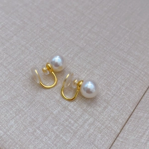 Detail view of 8mm pearl ear clips with golden metal U-shaped hooks and silicone pads