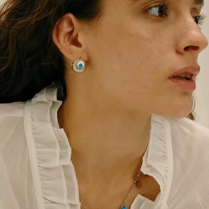Golden sunburst earrings with blue turquoise inlay worn by a model in a lifestyle setting