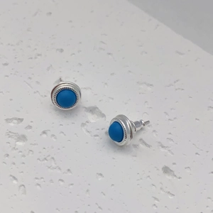 Close-up of silver round stud earrings featuring turquoise blue stones and textured edges