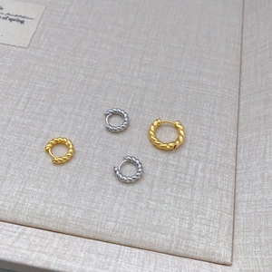 Braided twisted hoop earrings in gold and silver plating on textured fabric background