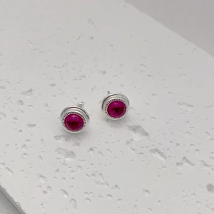 Detail of round silver earrings with rose red agate stone on white stone background