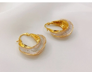 Macro detail of irregular gold-plated hoop earrings with white marble resin inlay