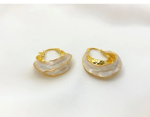 Detail of minimalist gold wavy earrings with white enamel finish and hammered texture