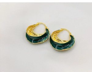 Detail of vintage C-shaped gold-plated copper earrings with deep green enamel texture