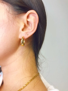 Detail of model wearing 18K gold plated thick hoop earrings with polished mirror finish