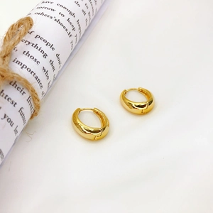 Detailed macro view of chunky gold hoop earrings with polished finish on white fabric