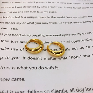 Macro shot of gold plated chunky hoop earrings with subtle engraving on a white book