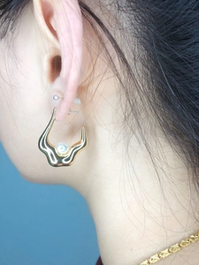 Detail of 18K gold-plated wavy earring with an inlaid white pearl on a model