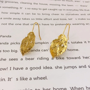 Vintage 18K gold plated leaf drop earrings with matte textured finish on a magazine