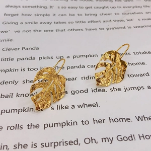 Macro detail of gold monstera leaf earrings with hammered texture on a book page