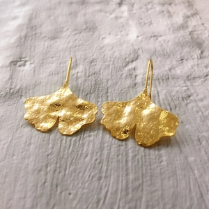 Textured gold ginkgo leaf dangle earrings on a natural stone surface backdrop
