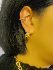 Close-up of golden oval hoop earrings and layered ear cuff worn on model's ear