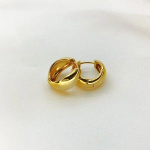 Macro shot of chunky oval gold hoop earrings on soft white textured fabric