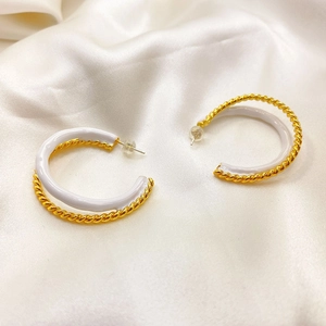 Gros plan de boucles d'oreilles torsadées en or 18 carats avec émail blanc sur soie