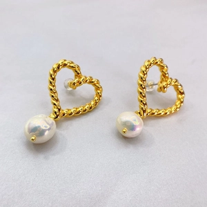 Détail des boucles d'oreilles cœur dorées avec texture torsadée et perles baroques