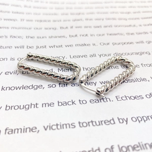 Detailed view of silver twisted rope hoop earrings with click-top closure on paper