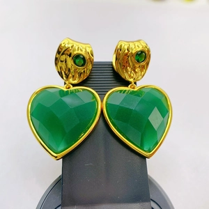 Macro view of gold plated heart earrings featuring faceted green gemstones in retro style