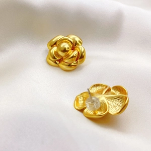 Goldene Kamelien-Ohrstecker mit gebürsteter Metalltextur auf weißem Seidenhintergrund