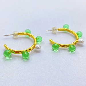 Boucles d'oreilles créoles dorées 18 carats avec perles vertes sur fond de sable