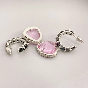 Détail de boucles d'oreilles argentées avec pierres cœurs roses et pavage noir subtil