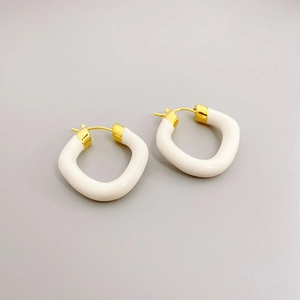 Modern gold-plated earrings with cream enamel finish on a neutral gray background