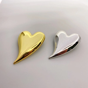 Asymmetric heart-shaped metal brooches in polished 18K gold and silver finishes