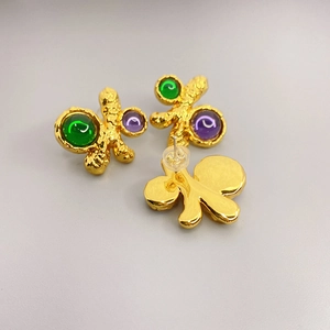 Irregular textured gold stud earrings with green and purple gemstones in top-down view