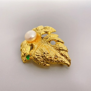 Detail of gold leaf brooch with cultured pearl and green gemstone on light gray background