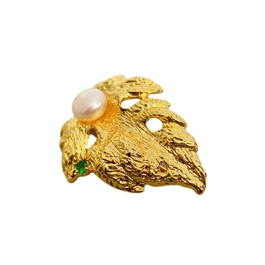 Golden leaf brooch with white cultured pearl and green gemstone on white background