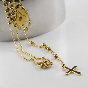 Detail view of a gold-tone cross pendant on a beaded chain draped over a metallic edge